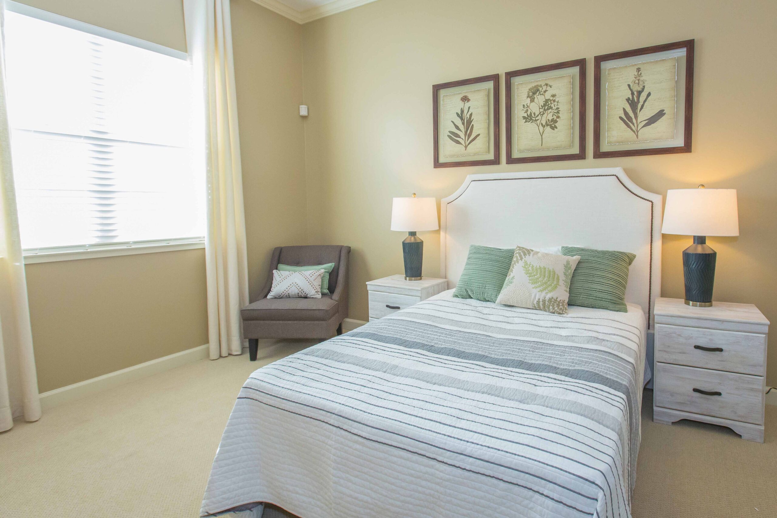 Sage Desert Tucson AZ 2018 June -0095 - The Ranch Estates of Tucson A bedroom with a made-up bed with white sheets, green pillows, two bedside tables with lamps on them, and a gray sofa chair with throw pillows in the corner.