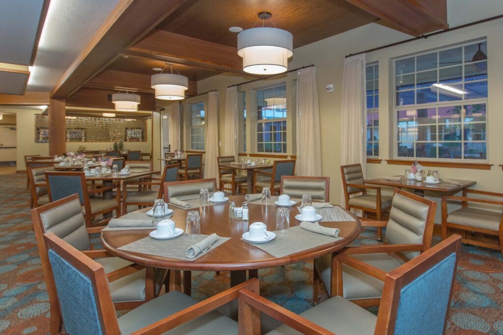 Sage Desert Tucson AZ 2018 June -0446 - The Ranch Estates of Tucson The Ranch Estates of Tucson dining area with circular brown tables, blue cushioned chairs, gray placemats and napkins, white cups, and glasses.