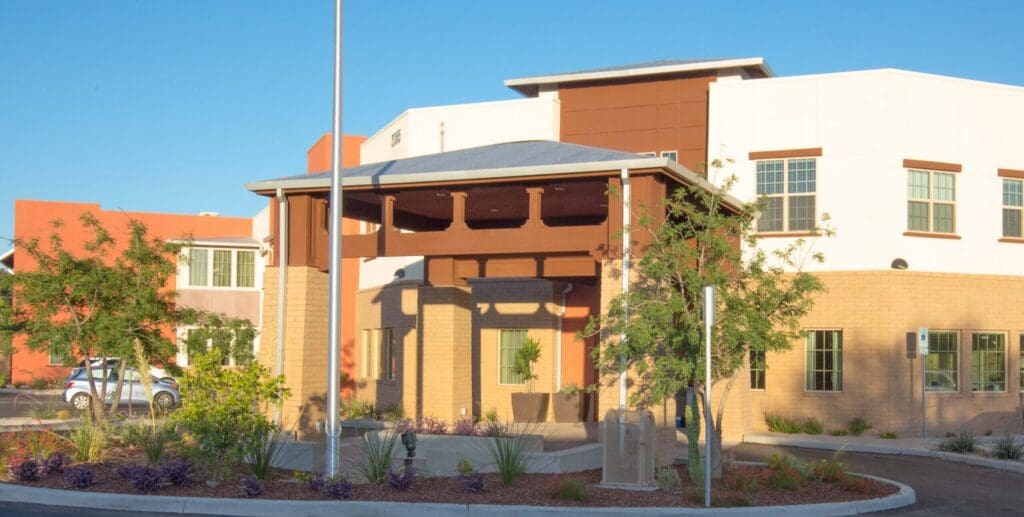 The Ranch Estates of Tucson front building with orange and white walls and little green trees in front of the driveway.